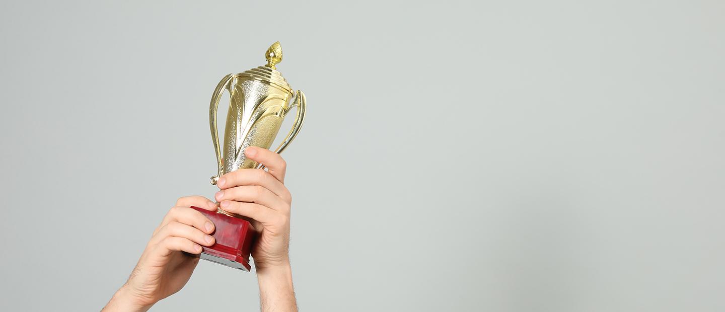 Hands holding up a gold trophy.